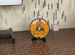 鳥のオオバンとカモがデザインされたオレンジ色の消火栓用鉄蓋が展示されている様子